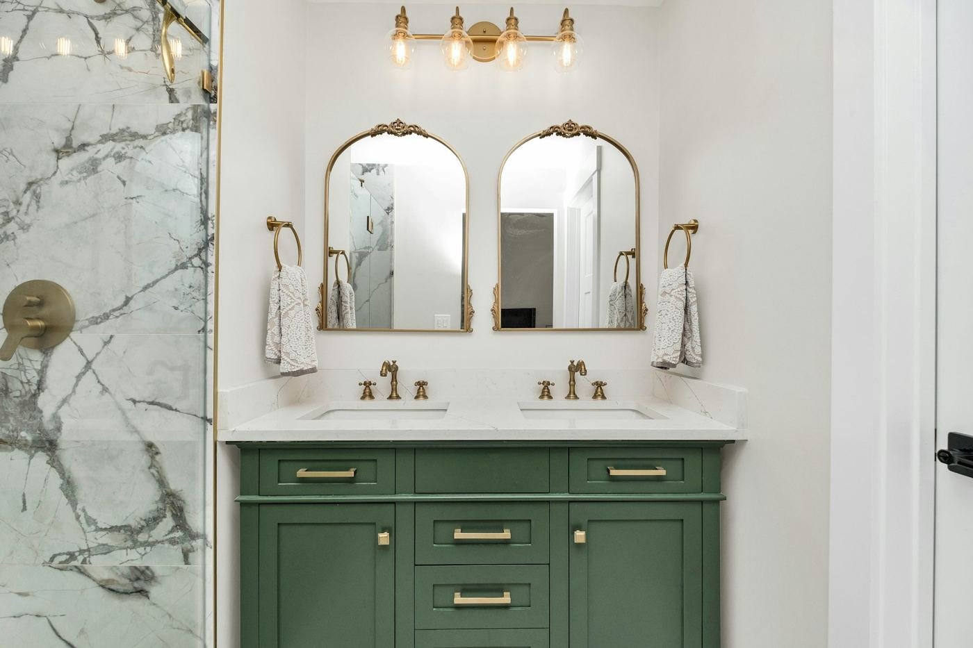 Remodeled bathroom with marble vanity, brass fixtures and green cabinets