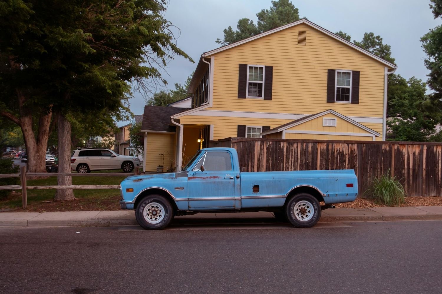 Blue pickup truck parked outside a two-story yellow suburban home
